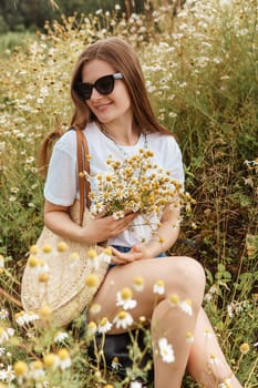 Beautiful young woman in nature with a bouquet of daisies. Field daisies, field of flowers. Summer tender photo.