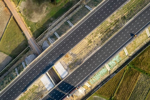 aerial drone shot moving along and shooting straight down of new delhi mumbai jaipur express elevated highway showing six lane road with green feilds with rectangular farms on the sides
