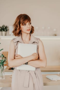 Brunette macbook. Portrait of a woman, she holds a mabuk in her hands, wearing a beige dress on a beige background