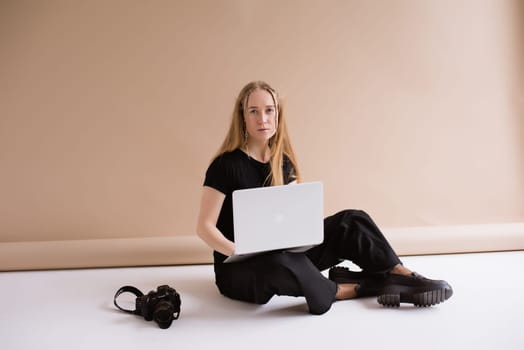 A business woman freelancer in a black is working, typing on a laptop apple and sitting on a white floor. blonde assistant in video production with computer MacBook and camera