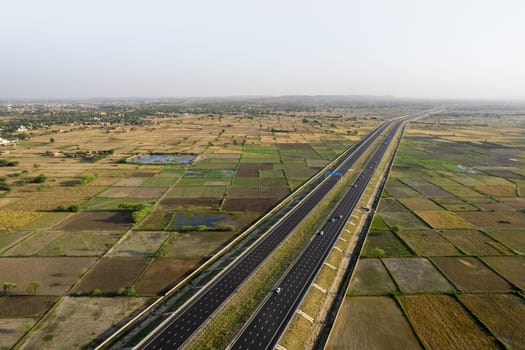 locked tripod aerial drone shot of new delhi mumbai jaipur express elevated highway showing six lane road with green feilds with rectangular farms on the sides