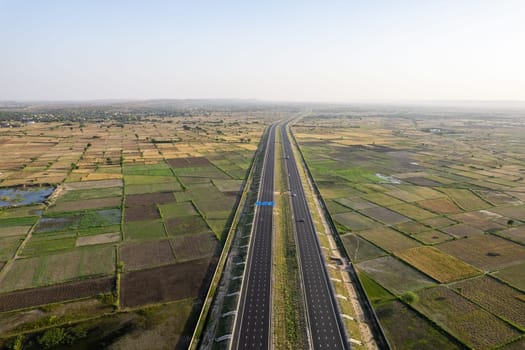 orbit aerial drone shot of new delhi mumbai jaipur express elevated highway showing six lane road with green feilds with rectangular farms on the sides