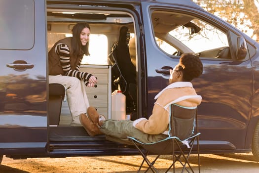 two young women chatting and having fun in a camper van at sunset, concept of travel adventure and weekend getaway with best friend