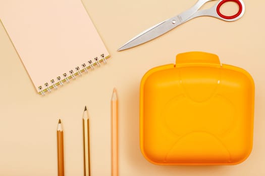 School supplies. Notebook, scissors, color pencils and lunch box on beige background. Top view. Back to school concept. Pastel colors