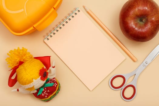 School supplies. Notebook, pencil,scissors, lunch box, apple and doll on beige background. Top view with copy space. Back to school concept. Pastel colors.