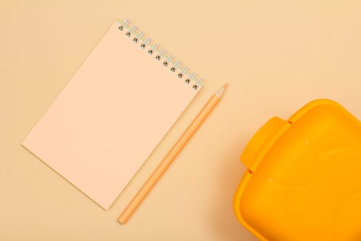School supplies. Notebook, color pencil and lunch box on beige background. Top view. Back to school concept. Pastel colors.