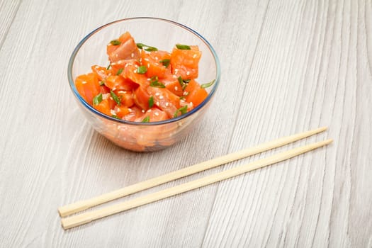 Hawaiian salmon poke with green onions and sesame seeds in glass bowl with chopsticks. Top view with copy space. Organic seafood.
