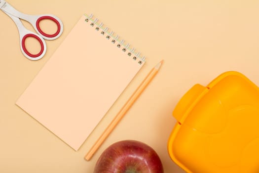 School supplies. Notebook, color pencil, apple, scissors and lunch box on beige background. Top view. Back to school concept. Pastel colors.