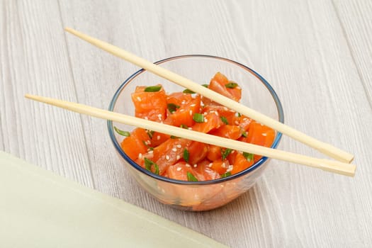Hawaiian salmon poke with green onions and sesame seeds in glass bowl with chopsticks. Top view. Organic seafood.