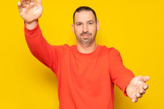 You did it. Congratulations. Happy cheerful positive hispanic man with beard standing over yellow colored background looking at camera, smiling and opening arms for warm hug