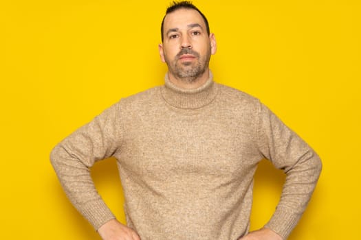 Cheerful bearded man wearing a red sweater posing isolated on gray background, studio portrait. People lifestyle concept. Mock up copy space. Standing with arms akimbo on waist blinking.