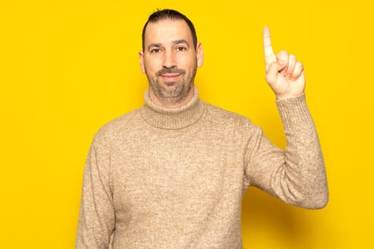 Insightful smart proactive caucasian man 40s wearing a turtleneck holding index finger up with a great new idea isolated on yellow background studio portrait. People lifestyle concept