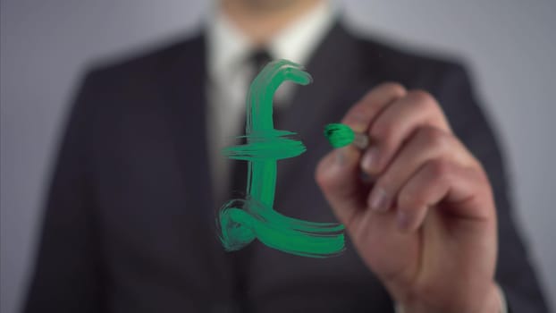 A businessman draws the Pound Sterling symbol on the glass. A man in a suit draws on glass with a brush and green paint. 4k