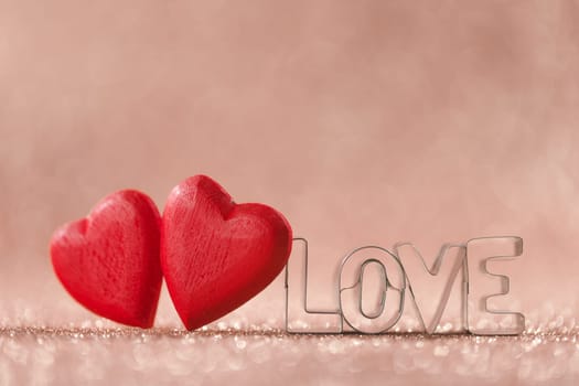 Two red handmade wooden hearts and word love on pink bright glitter lights bokeh background