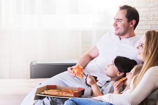 Happy family eating pizza while watching TV on sofa at home