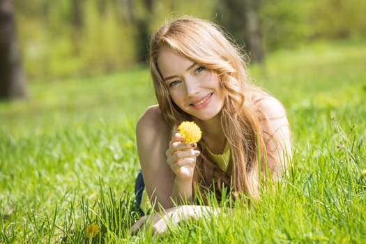 Portrait of young smiling woman on the grass holding dandelion flower