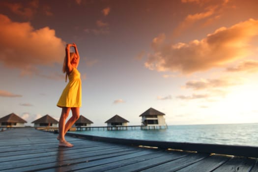 woman in a dress on a bridge home sea and the maldivian sunset on the background