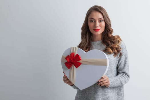 Young girl with heart-shaped gift box on white background