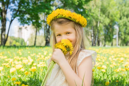 Little girl enjoys the smell of flowers in the meadow