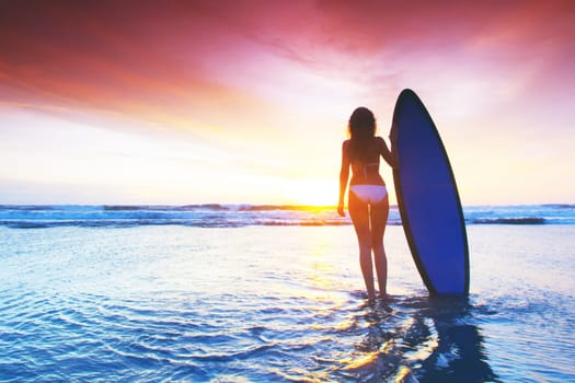 Beautiful surfer woman on the beach at sunset