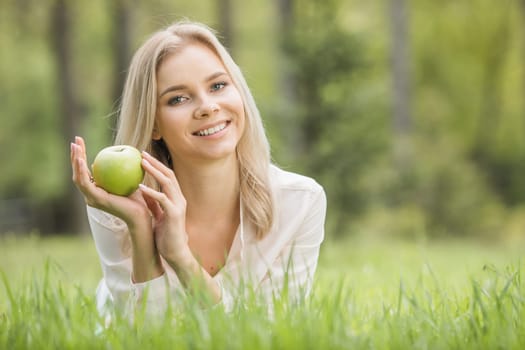 Woman with apple laying on green grass, background with copy space