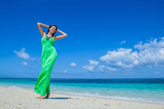 Beautiful young woman in green dress dancing at sea beach