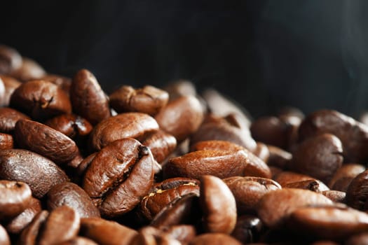 Hot roasted coffee beans and steam on black