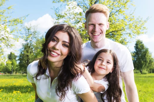 Happy family having fun outdoors in spring park against natural green meadow and trees background
