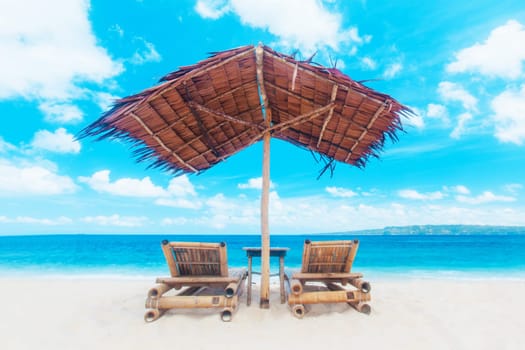Two chaise lounges and straw umbrella on tropical beach