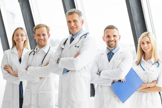 Successful team of medical doctors are looking at camera and smiling while standing with arms crossed in hospital