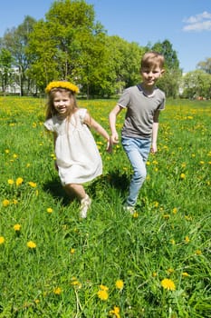 Happy children friends run and play outdoors on yellow dandelion flower meadow