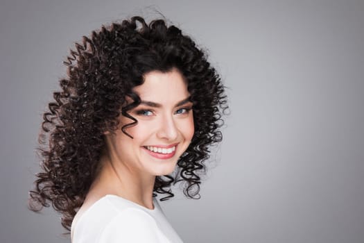 Studio portrait of beautiful smiling woman with curly dark hair on gray background