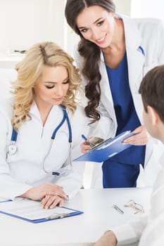 Female doctor , her assistant and patient filling forms in medical clinic office