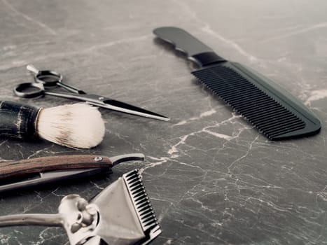 On a grey marble surface are old barber tools. Vintage manual hair clipper comb razor shaving brush shaving brush hairdressing scissors.