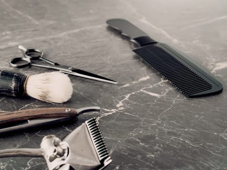 On a grey marble surface are old barber tools. Vintage manual hair clipper comb razor shaving brush shaving brush hairdressing scissors.