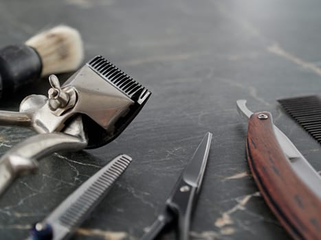 On grey marble surface are old barber tools. Vintage manual hair clipper comb razor shaving brush shaving brush hairdressing scissors.