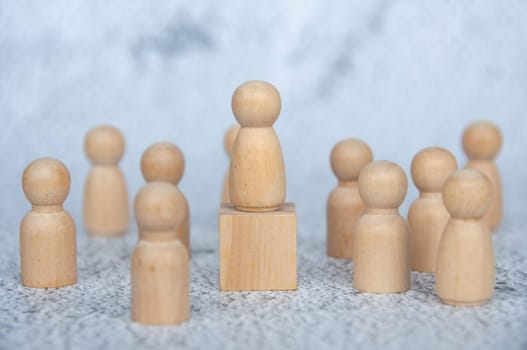 A wooden figure on top of wooden block representing a leader surrounded by other wooden figure. Leadership concept.