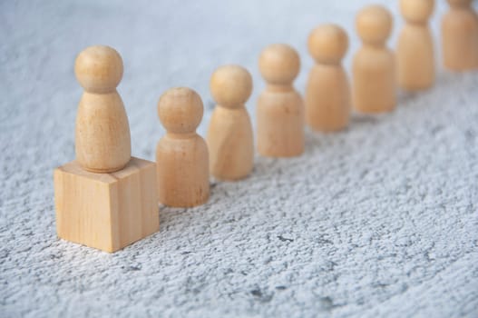 A wooden figure on top of wooden block representing a leader leading other figure. Leadership concept