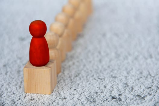 Red wooden figure on top of wooden block representing a leader leading other figure. Leadership concept.