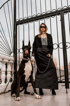 A woman walks with her Great Dane in an urban setting, enjoying the outdoors and the company of her dog