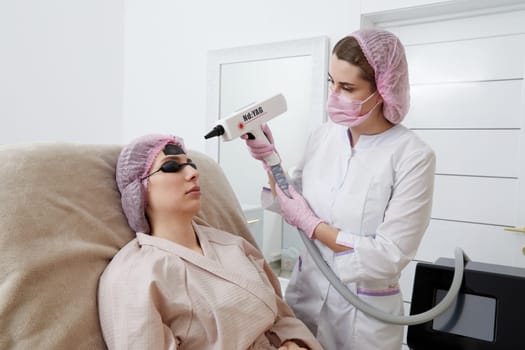 Carbon peeling in beauty salon. Cosmetologist applying black mask on the face of beautiful woman for carbon peeling