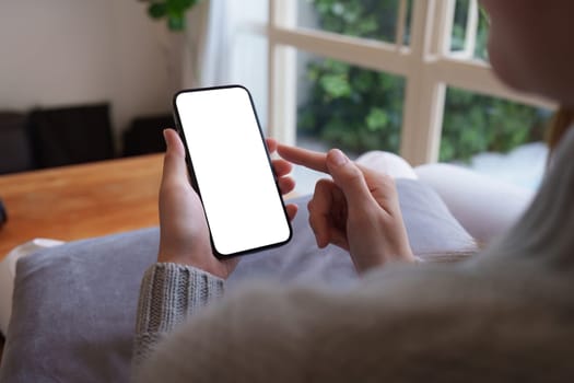 Close up woman hand holding a smartphone blank white screen sitting on sofa at home.
