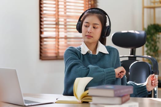 Online education, e-learning. Asian woman relaxing after studying using a laptop, listening to online lecture, taking notes, online study at home.