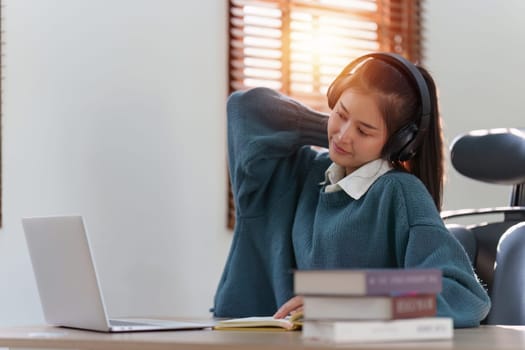 Online education, e-learning. Asian woman relaxing after studying using a laptop, listening to online lecture, taking notes, online study at home.