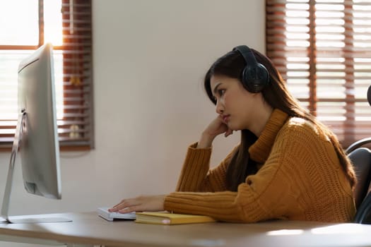 Online education, e-learning. Asian woman relaxing after studying using a laptop, listening to online lecture, taking notes, online study at home.