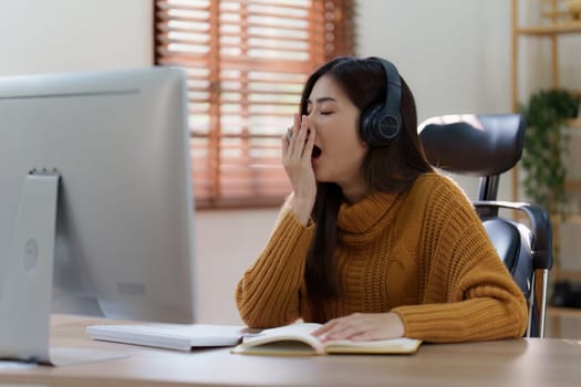 Online education, e-learning. Asian woman relaxing after studying using a laptop, listening to online lecture, taking notes, online study at home.