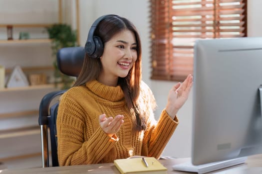 Asian woman having video call on her computer at home. listening to online lecture, taking notes, online study at home.