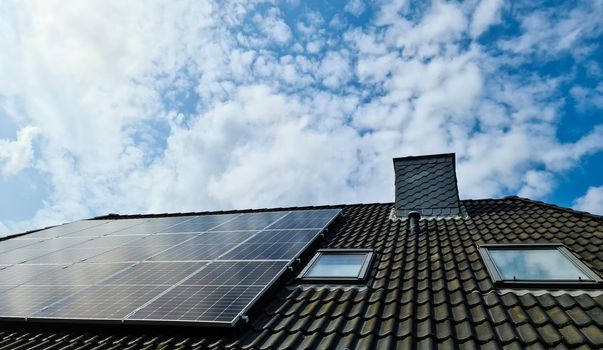 Solar panels producing clean energy on a roof of a residential house with cloud reflections