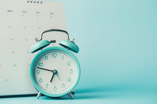 An alarm clock with calendar on blue background for the concept of time and date management.