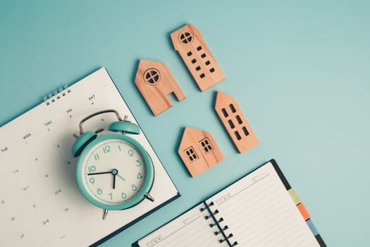 An alarm clock with calendar, notebook and wooden house model for the concept of time management, housing and property.